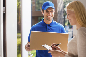 Signing for the package. Smiling young delivery man holding a cardboard box while beautiful young woman putting signature in clipboard
